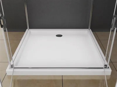 A close-up view of a white shower tray with a drain hole, framed by glass shower doors and metal supports.