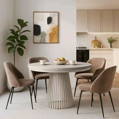 A dining room setting with a round table and chairs, a plant, and a painting on the wall.