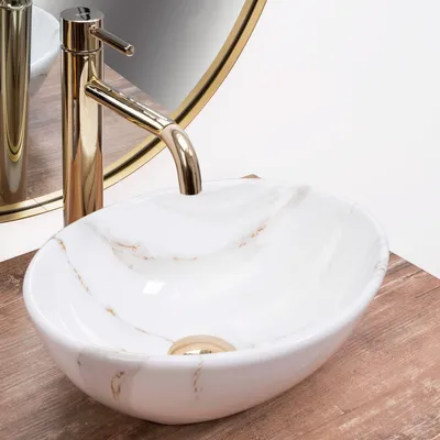 A close-up view of a marble-patterned vessel sink with a gold faucet, placed on a wooden surface.