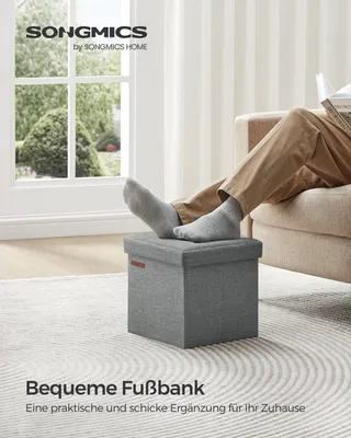 A person's legs and feet are resting on a gray storage ottoman in a living room setting.