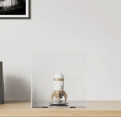 A clear acrylic display case containing a decorative rocket figurine.