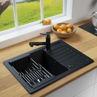 A black kitchen sink with a drying rack and faucet, set on a wooden countertop next to a window with a view of a green landscape.