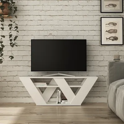 A modern white TV stand with a television on top, placed against a white brick wall.