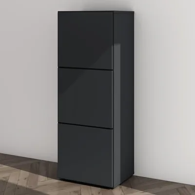 A dark gray shoe cabinet with three drawers stands against a light gray wall, with a wooden floor in the foreground.
