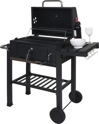 A black charcoal grill with its lid open, placed on a white background. Accessories like a wine bottle, a bowl, and a wine glass are placed on the side table.