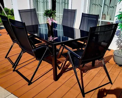 A black aluminum garden furniture set with a glass-top table and chairs on a wooden deck.