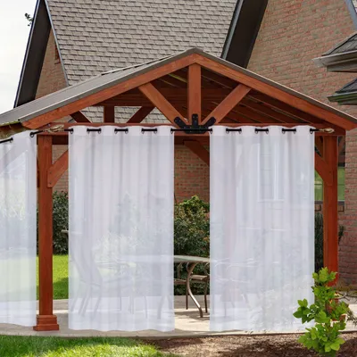 White outdoor curtains are hanging from a wooden gazebo, with a table and chairs visible in the background.