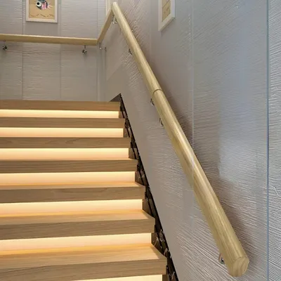 A wooden handrail runs along a modern staircase with illuminated steps.