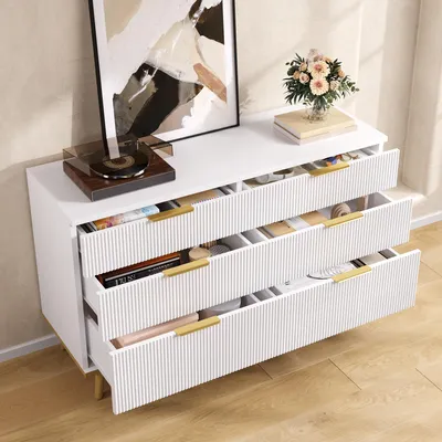 A white dresser with open drawers, displaying various items inside, placed against a textured wall.