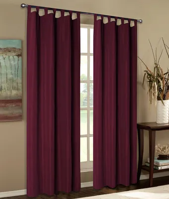 Two burgundy curtains are hanging in front of a window, with a small table and decorative items to the right.