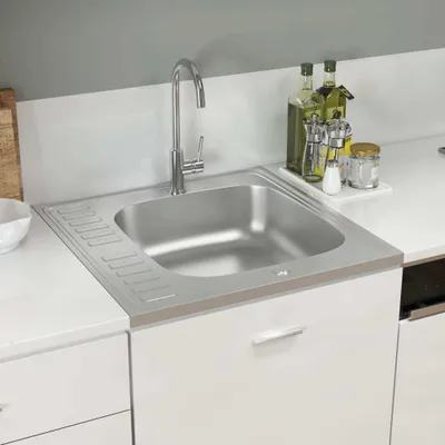 A stainless steel kitchen sink with a drainboard, faucet, and some bottles of oil and seasonings on the countertop.