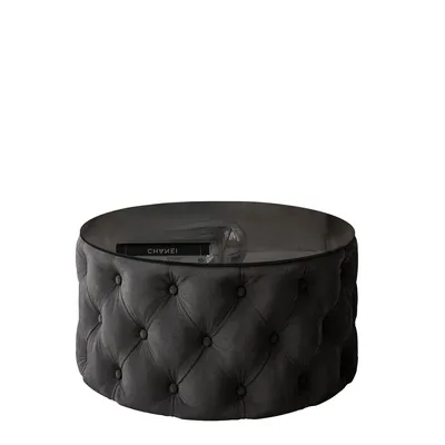 A round, tufted ottoman with a glass top, displaying a book and a glass.