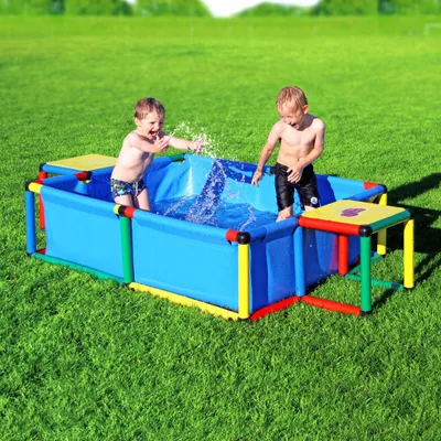 Two young children are playing in a blue paddling pool filled with water, set up on a green grassy lawn.