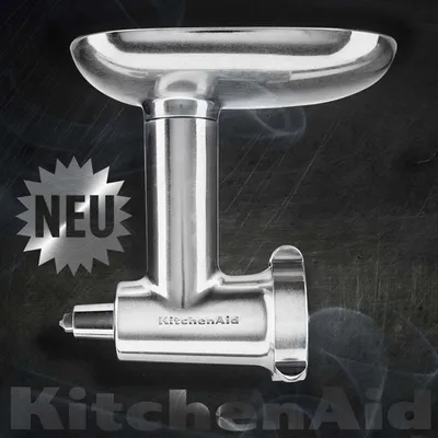 A KitchenAid meat grinder attachment is presented against a smoky, dark background, with the 'NEU' (New) badge and KitchenAid logo prominently displayed.