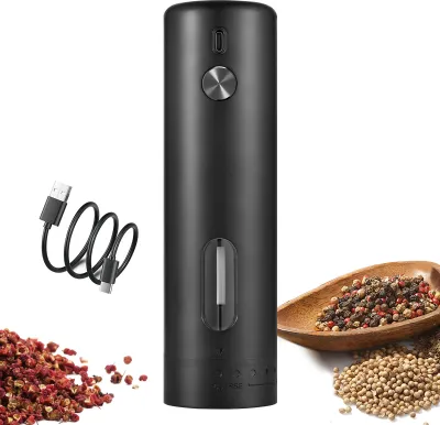 A black electric pepper grinder with a USB charging cable and a pile of peppercorns and other spices.