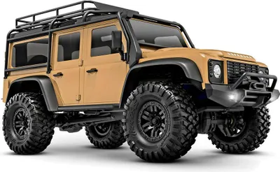 A tan Traxxas TRX-4M Land Rover Defender RC car is shown from a three-quarter front angle against a white background.