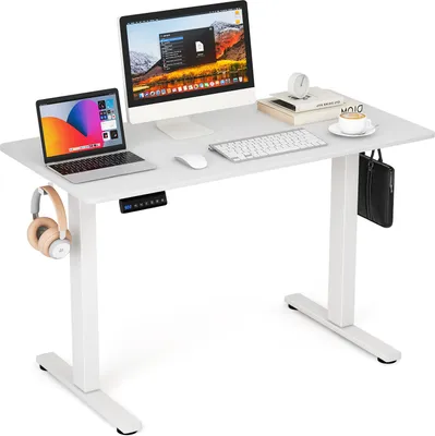 A white adjustable standing desk with a laptop, monitor, keyboard, mouse, headphones, and a bag.