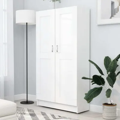 A white two-door cabinet is shown in a room with a floor lamp and a potted plant.
