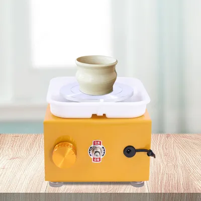 A small yellow pottery wheel with a beige pot on top, placed on a wooden surface.