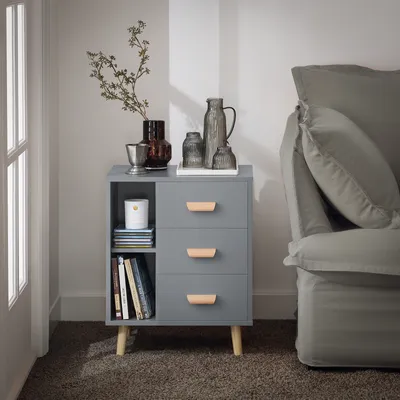 A gray nightstand with three drawers and an open shelf, placed next to a gray sofa in a room.