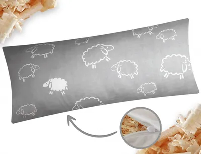 A long pillow with a sheep pattern is shown on a light gray background, with wood shavings scattered around the edges. A close-up inset shows the zipper and filling of the pillow.