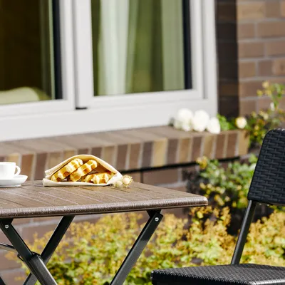 A small wooden-look table with a cup of coffee and waffles on it, set up outdoors.