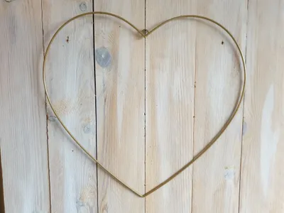 A gold metal heart-shaped decoration is placed on a light-colored wooden background.