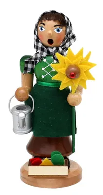 Die Gärtnerin trägt eine Kleid und einer grünen Schürze, sowie ein kariertes Kopftuch.