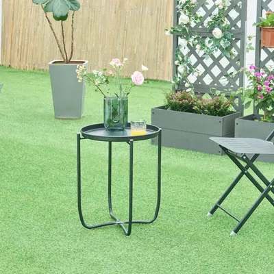 A small round black table with a vase of flowers and a glass on it, set on a green lawn with planters and a trellis in the background.