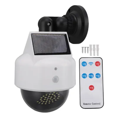 A solar-powered surveillance camera dummy with a remote control, screws, and wall plugs, displayed on a white background.