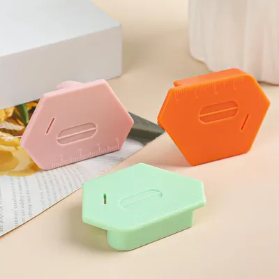 Three hexagonal magnetic seam guides in pink, orange, and green are displayed on a surface with a blurry background. One is slightly in front of the other two.