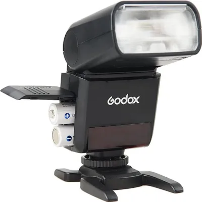 A black Godox TT350O camera flash unit with batteries visible, mounted on a stand.