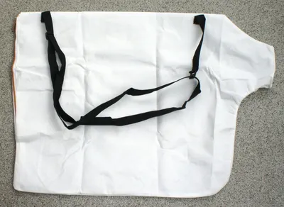 A white fabric bag with black straps laid flat on a gray surface.