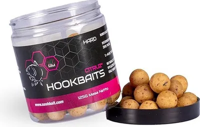 A jar of fishing bait (hookbaits) is shown tilted, with some bait balls spilled out in front of it.