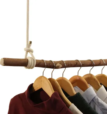 A rustic wooden branch used as a clothes rack, with several wooden hangers holding clothes.