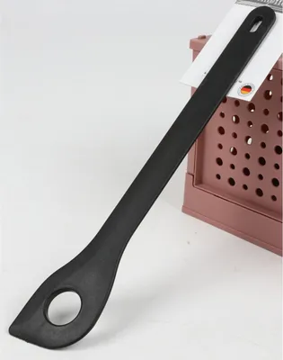 A black kitchen utensil with a hole in the handle rests on a pink grid-like surface.