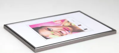 A framed picture of a woman with colorful makeup and nails, displayed on a white surface.