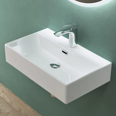 A white ceramic sink with a chrome faucet is mounted on a green wall. Part of a wooden surface is visible in the foreground.