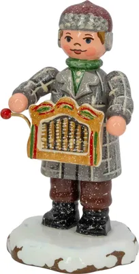 Ein fröhlicher Drehorgelspieler in winterlicher Kleidung steht auf einer schneebedeckten Basis und hält eine bunte Drehorgel in den Händen während er freundlich lächelt