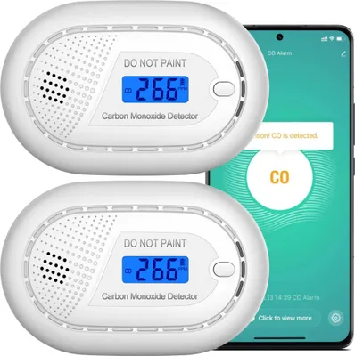 Two white carbon monoxide detectors are shown next to a smartphone displaying a CO alarm notification.