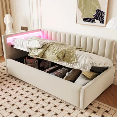 A beige upholstered daybed with storage is shown with its mattress pulled out, revealing storage compartments underneath. The daybed has pink LED lighting along the headboard.