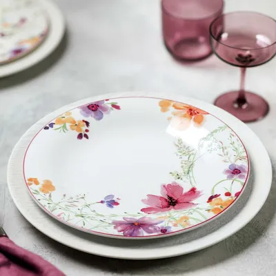 A floral patterned plate is shown on top of another plate, with two purple glasses in the background.