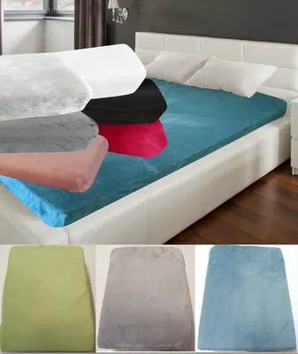 A bed with a teal fitted sheet and several folded fitted sheets in different colors stacked on top. Below are three folded fitted sheets in green, gray, and blue.