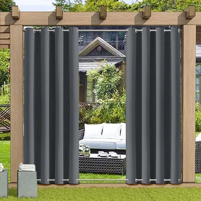 Outdoor curtains hanging on a pergola, framing a view of a house and patio furniture.