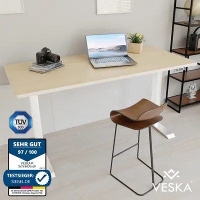A modern office setup with a standing desk, laptop, camera, and stool.