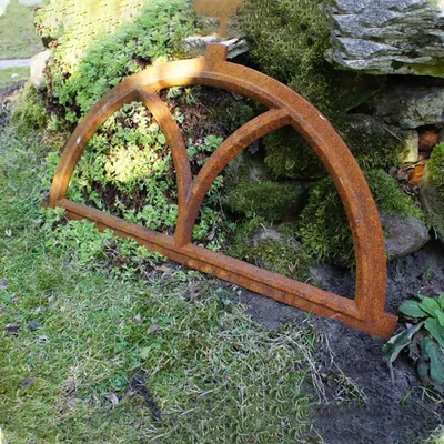 A rusty metal window frame lying on the ground in a garden setting, surrounded by grass, moss, and rocks.