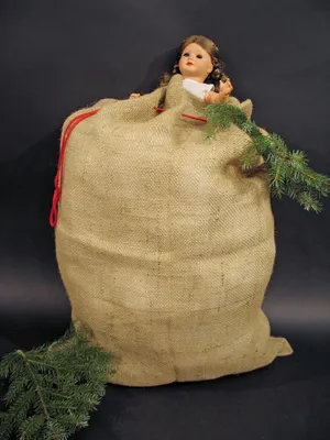 A large burlap sack with a doll and a Christmas tree branch sticking out of it, set against a black background.