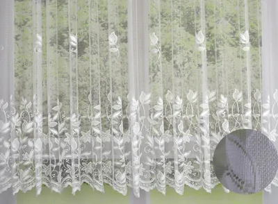 A white lace curtain with a floral pattern hanging in front of a window with greenery visible outside.