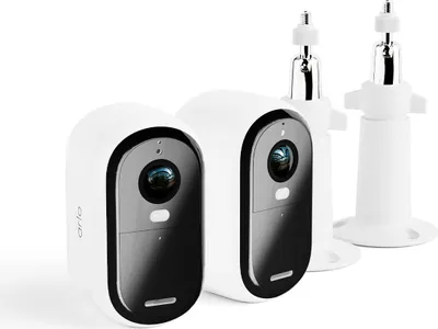 Two white Arlo Essential 2 FHD Outdoor Cameras with black accents are shown in the foreground, along with two white wall mounts in the background.