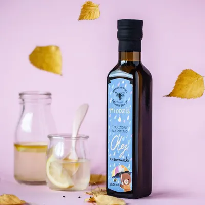 A bottle of oil with a label, next to a glass of lemon water and a small bottle. Autumn leaves are scattered around.